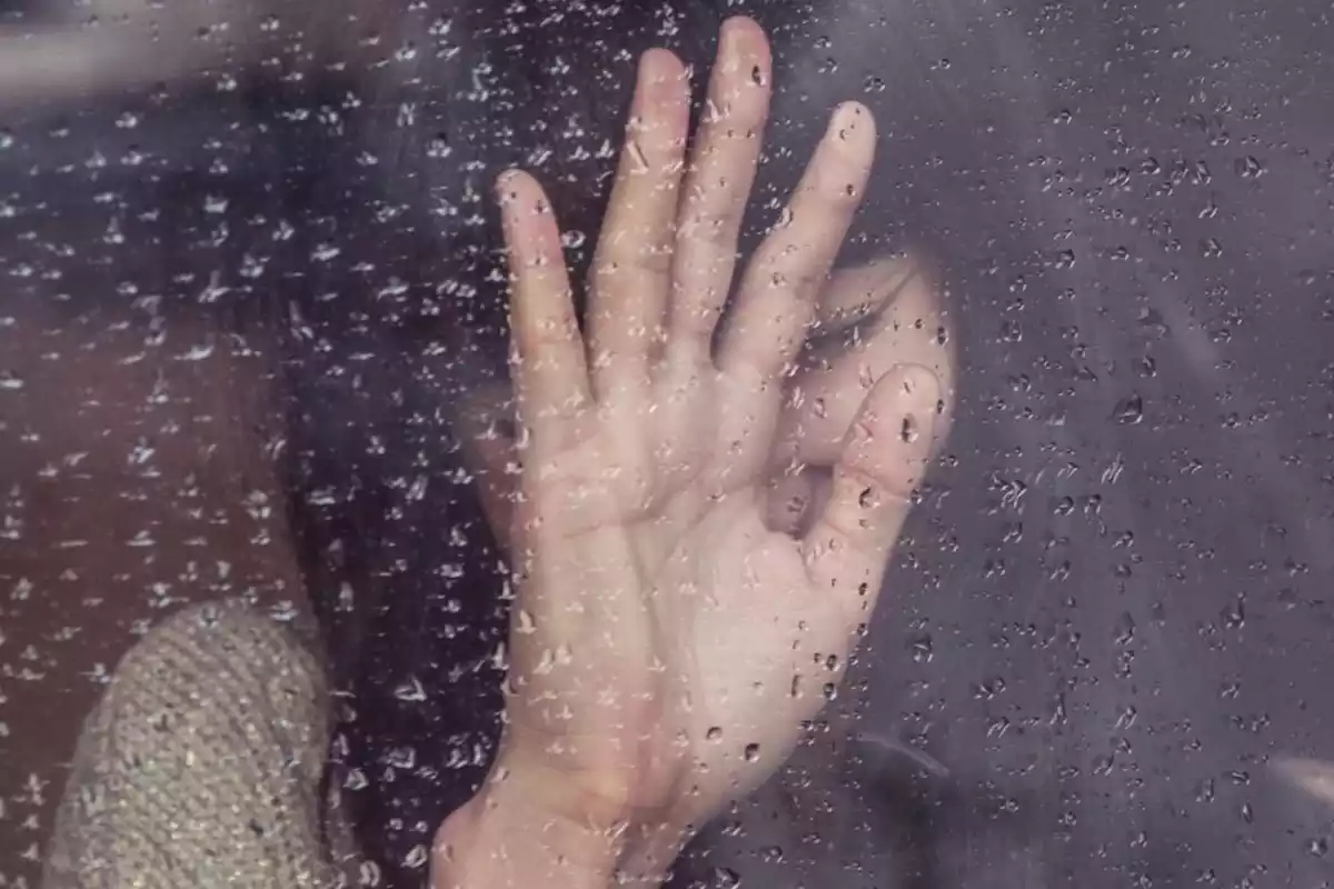 Imagen de una chica apoyada en un cristal mojado