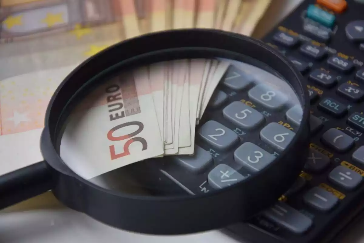 Una lupa encima de unos cuantos billetes de cincuenta euros y una calculadora