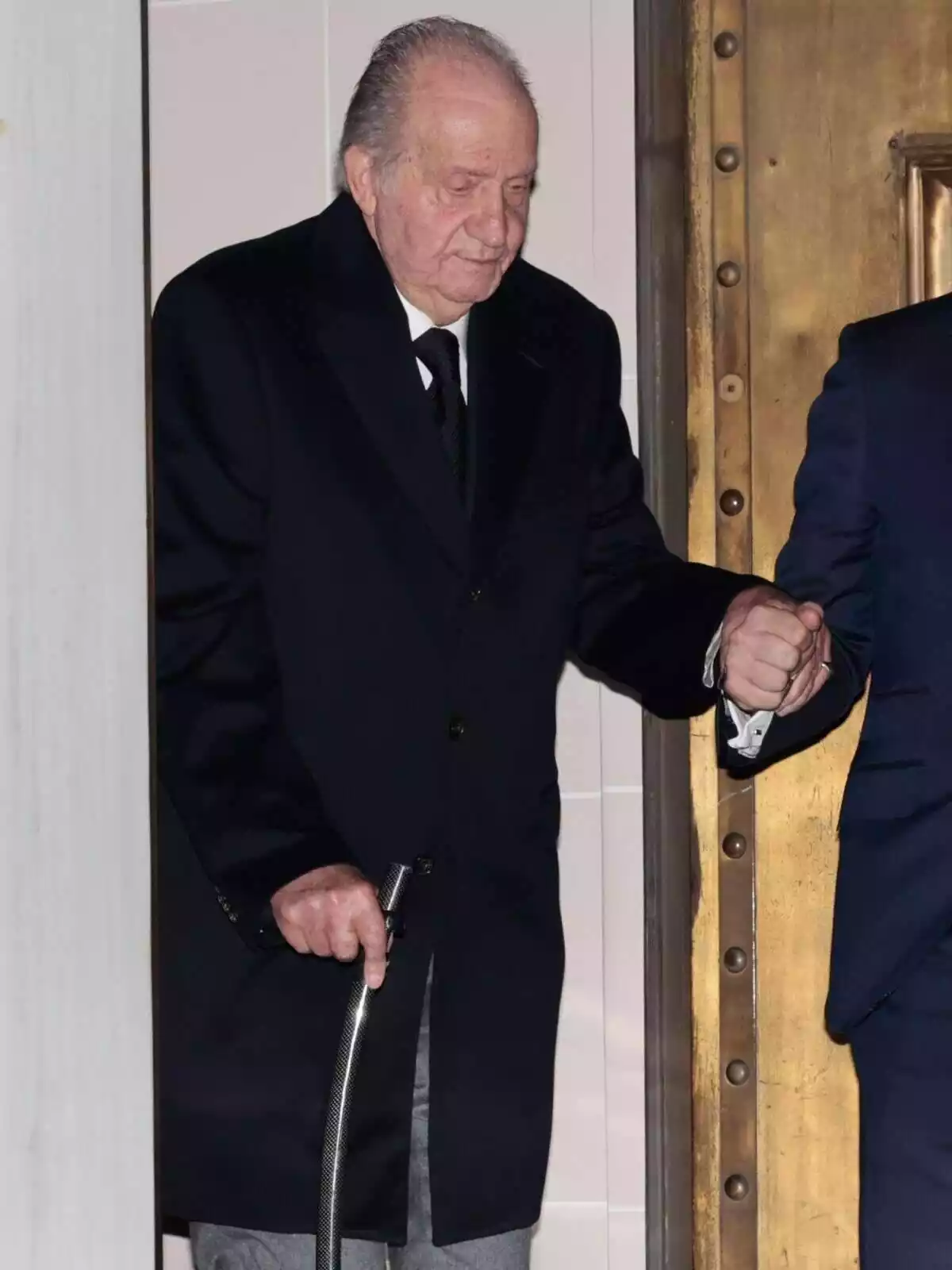El Rey Juan Carlos I andando con la ayuda de un bastón y de un hombre El Rey Juan Carlos I andando con la ayuda de un bastón y de un hombre